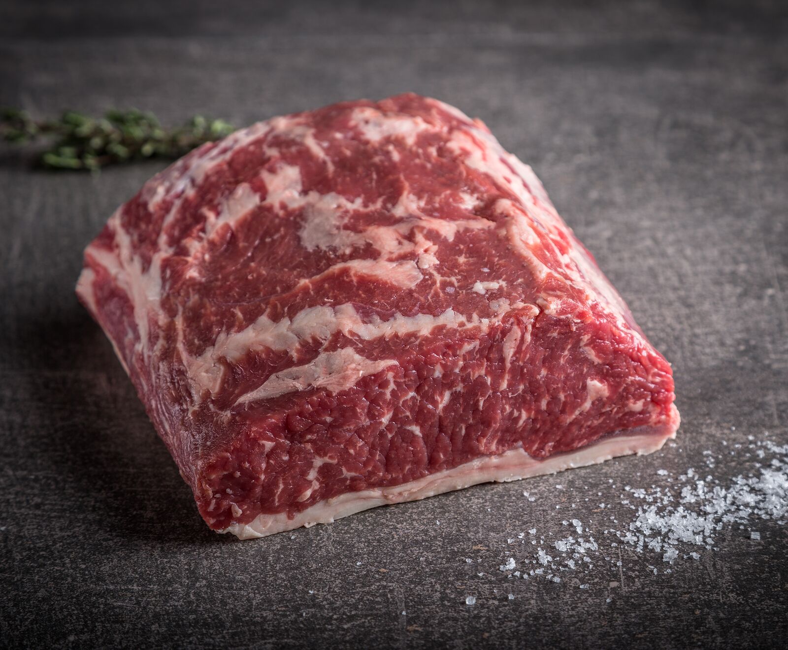 Rohes Stück Rindfleisch mit Fettmarmorierung und Salz auf dunklem Hintergrund.